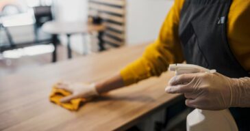 side-view-female-barista-cleaning-table-while-wearing-latex-gloves_23-2148522930